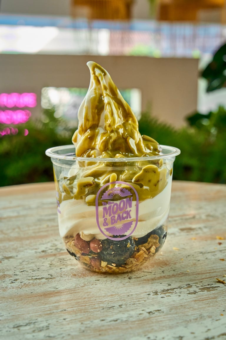 Pistachio soft serve ice cream in a clear cup with graham cracker base and purple Snack Pack label, on outdoor wooden surface