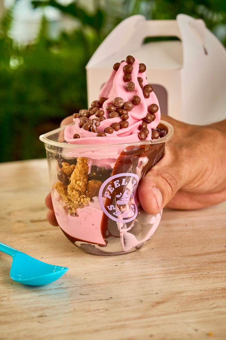 Hand holding pink frozen yogurt topped with granola and chocolate chips outdoors