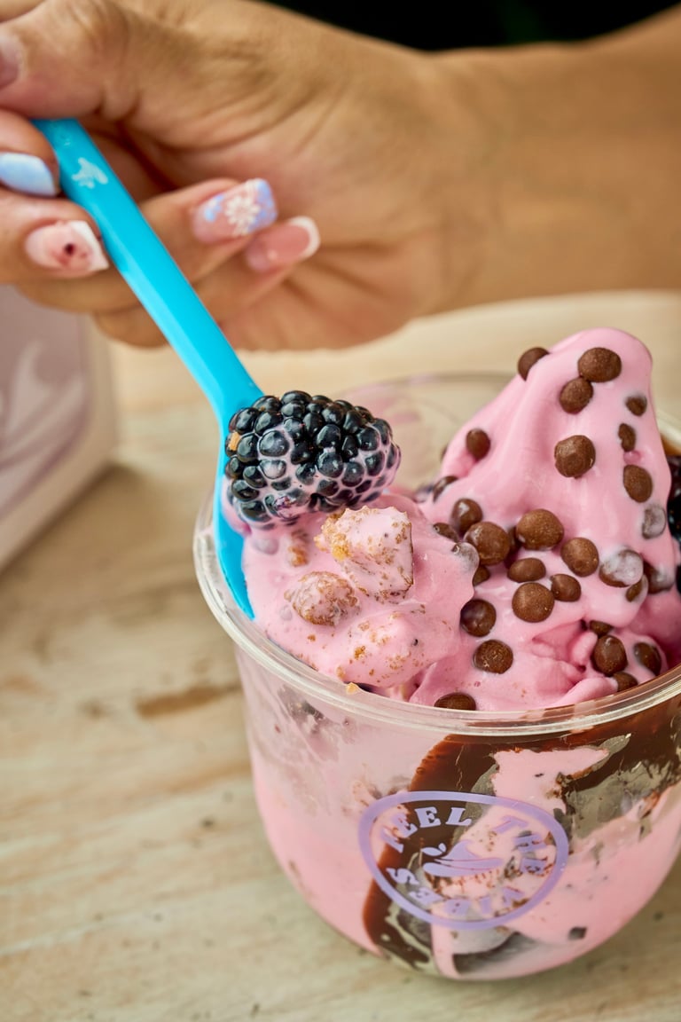 Hand holding pink ice cream with chocolate chips and blackberries in a clear cup
